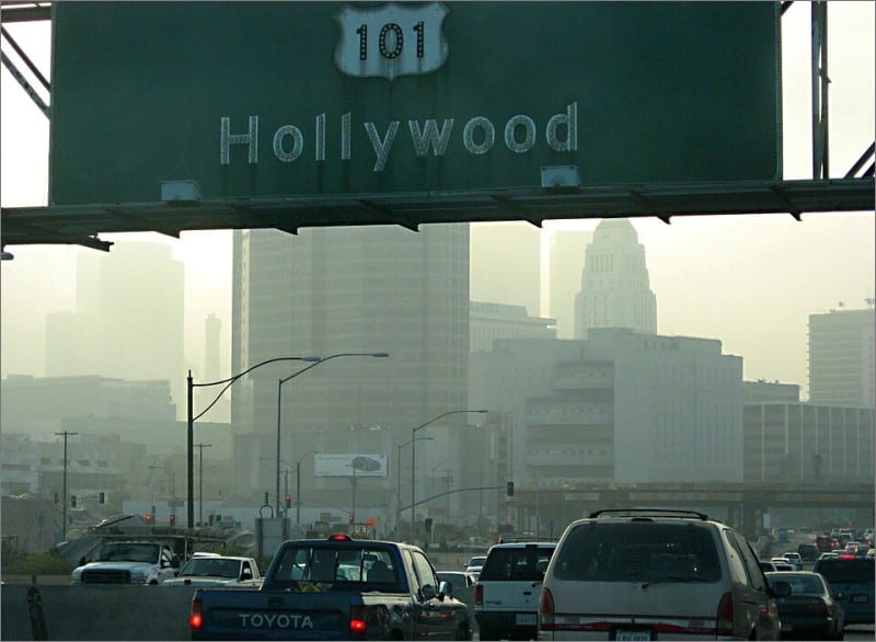 Smoggy downtown Los Angeles skyline behind a US Route 101 Hollywood highway sign over heavy traffic