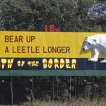 Yellow South of the Border billboard reading "Bear up a leetle longer, 16 mi" with a cartoon Mexican in a sombrero and a white polar bear
