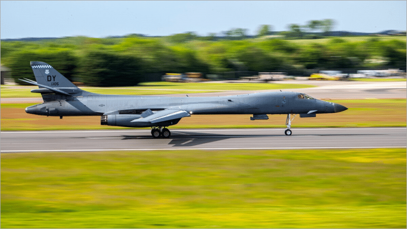 US Air Force B-1B Lancer bomber with a DY tail code rolling down the runway at RAF Fairford in England, green fields and trees behind it