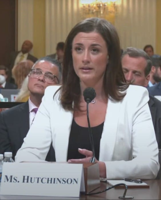Cassidy Hutchinson in a white blazer testifies at a microphone behind a “Ms. Hutchinson” nameplate at the June 28, 2022, January 6 committee hearing.